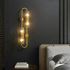 This Clérachic double brass wall light glows on a charcoal wall beside a grey upholstered bed and a nightstand with a stack of books.