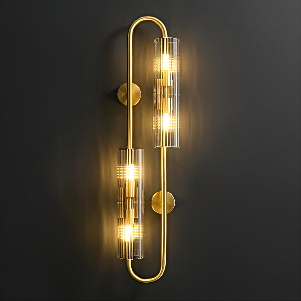 Lit close up, the ribbed glass tubes of this Clérachic brass wall light throw a warm glow across a dark wall from a looped brass frame.