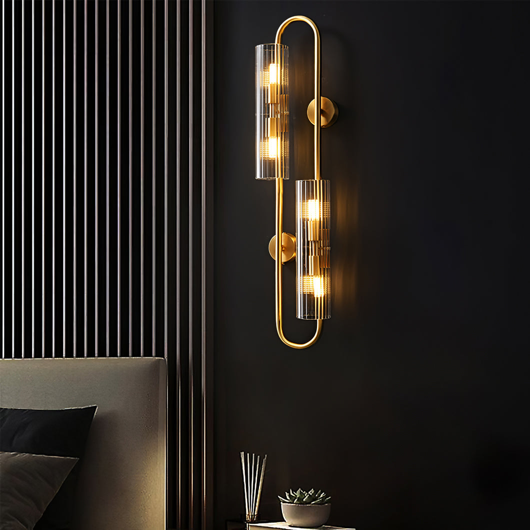 On a dark wall beside slatted panelling, this Clérachic brass wall light glows above a grey headboard and a small plant on a side table.