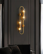 Lit on a dark panelled wall above dark cushions, this Clérachic double brass wall light has a tall looped frame and two glass tubes.