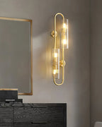 Over a black chest of drawers with a mirror in a brass frame, this Clérachic double brass wall light glows on a grey wall.