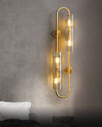 Lit on a rough grey plaster wall above a bed, this Clérachic brass wall light shows warm bulbs through its ribbed glass tubes.