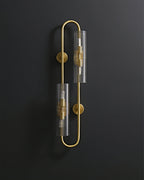 Unlit, this Clérachic brass wall light shows its two ribbed clear glass tubes and round wall plates against a dark background.