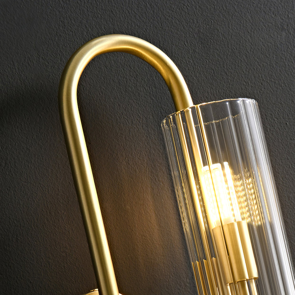 Close view of the ribbed glass tube and curved brass arm of this Clérachic wall light, with the bulb glowing inside.