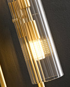 Close view of the vertical ribbing on the glass of this Clérachic wall light, with brass stacked fittings and a warm bulb inside.