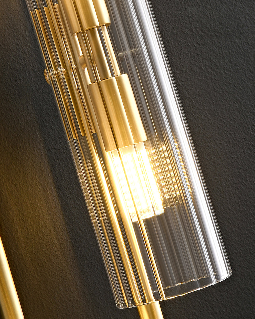 Close view of the vertical ribbing on the glass of this Clérachic wall light, with brass stacked fittings and a warm bulb inside.