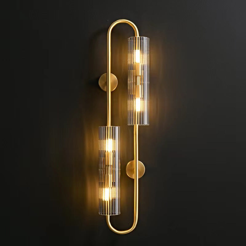 Straight-on view of this Clérachic brass wall light lit against a dark wall, the two tubes glowing warm on a looped frame.