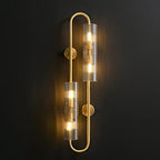 Straight-on view of this Clérachic brass wall light lit against a dark wall, the two tubes glowing warm on a looped frame.