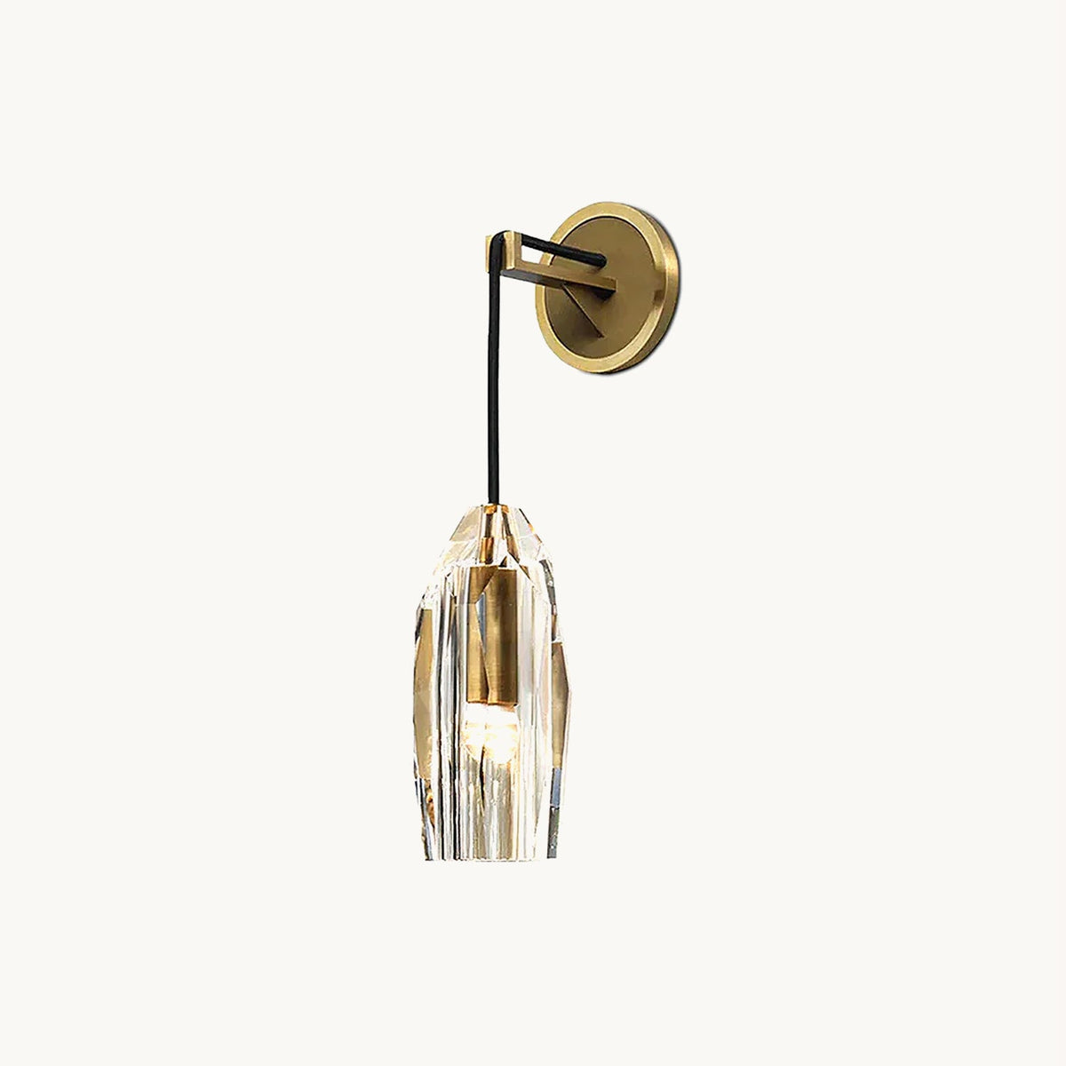 A Clérachic wall light on a plain white backdrop: a round brass backplate, a black cord arm and a faceted crystal shade with a brass socket inside.