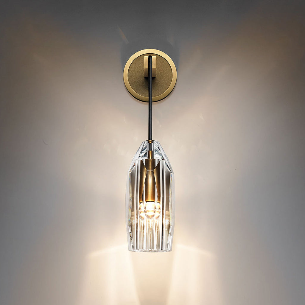 A lit Clérachic wall light on a dark, softly glowing wall, the clear crystal shade throwing bright streaks of light downward.