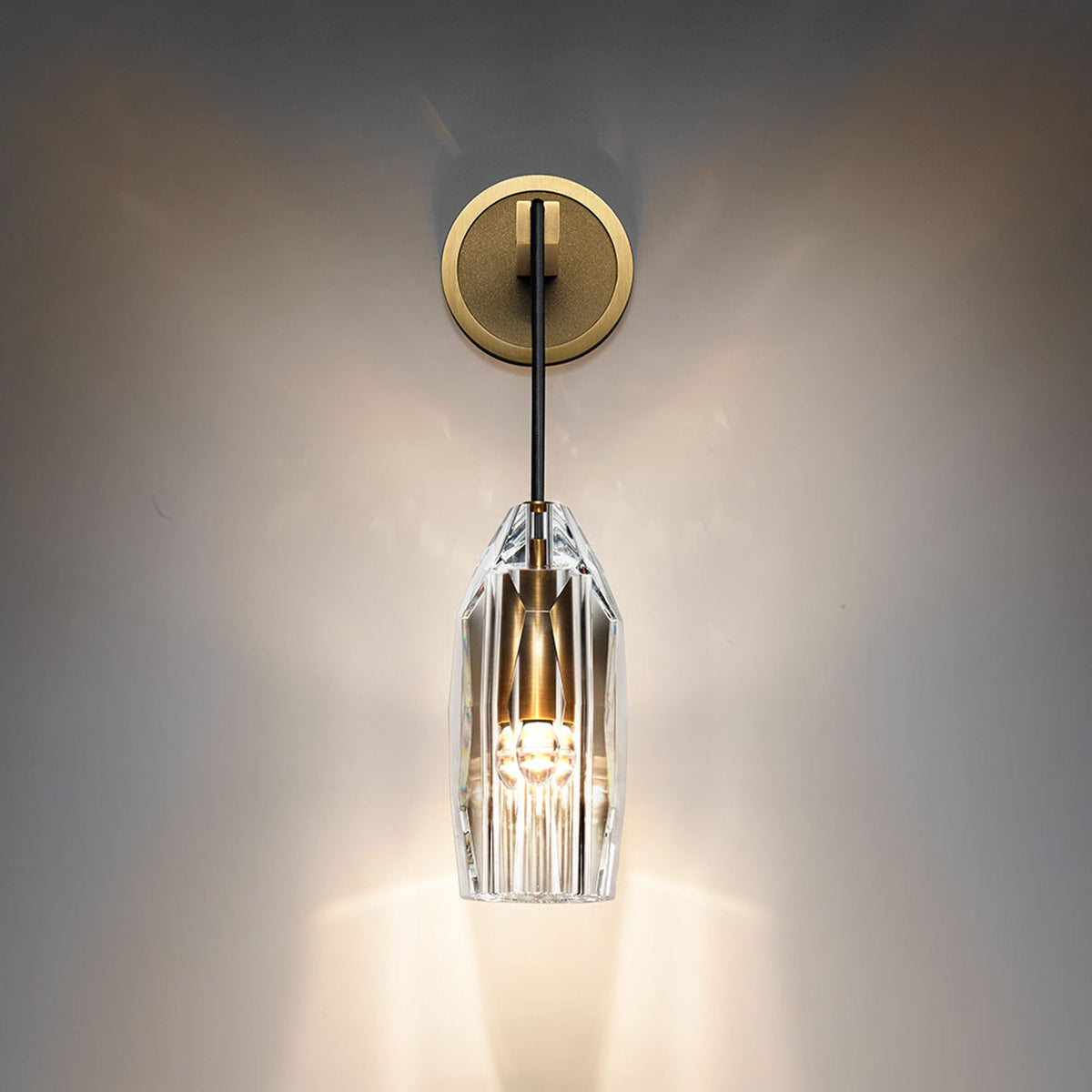A lit Clérachic wall light on a dark, softly glowing wall, the clear crystal shade throwing bright streaks of light downward.