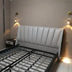 Two Clérachic crystal wall lights lit above a grey padded bed head, in a bedroom with a navy bedside table and an unmade slatted base.