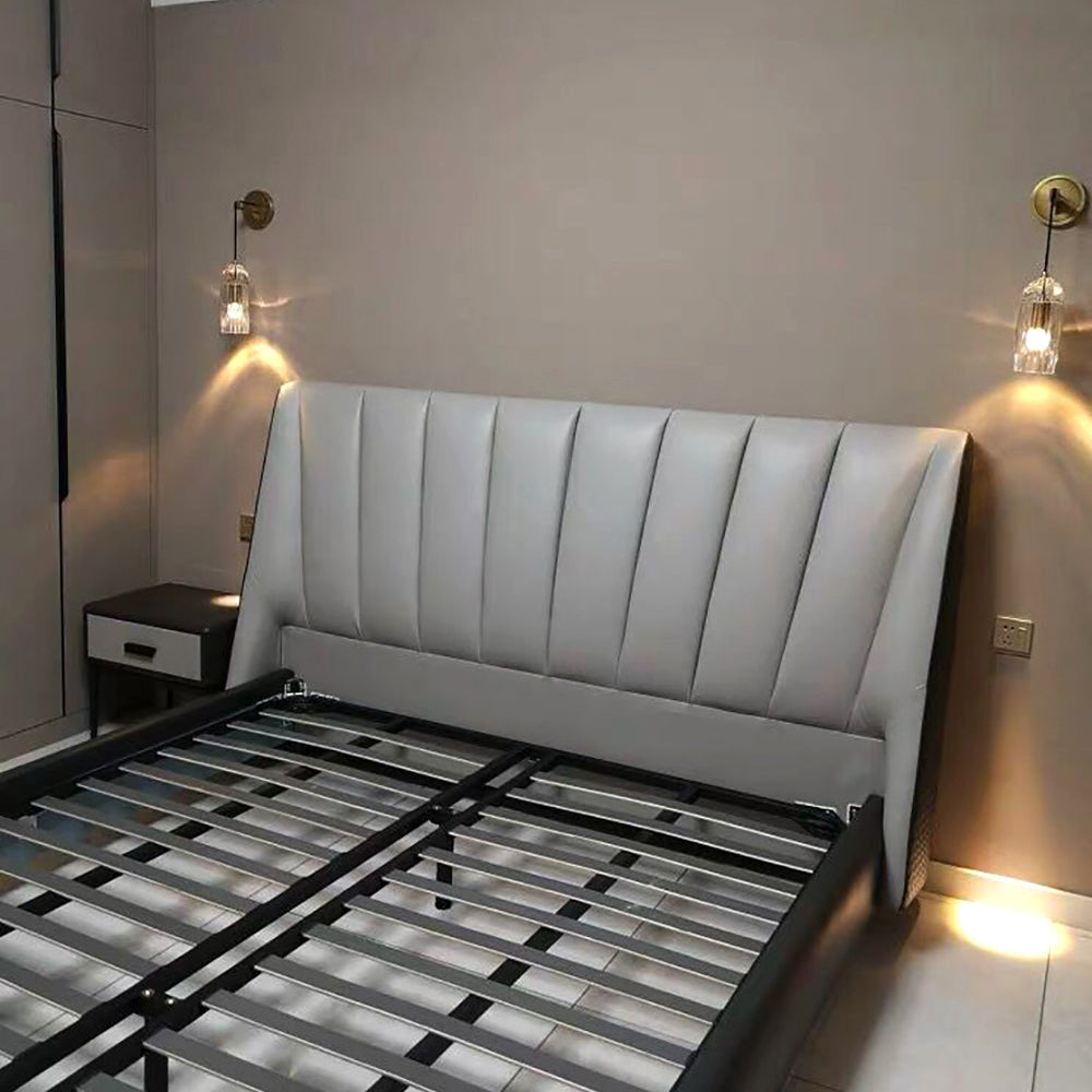 Two Clérachic crystal wall lights lit above a grey padded bed head, in a bedroom with a navy bedside table and an unmade slatted base.