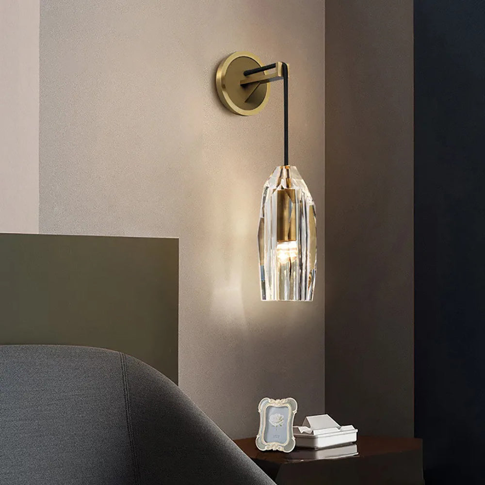 This Clérachic wall light beside a grey armchair and a dark side table with a framed photo, the crystal shade glowing softly.
