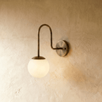 Clérachic wall lamp in vintage brass, a frosted glass globe glowing beneath a curved gooseneck arm.