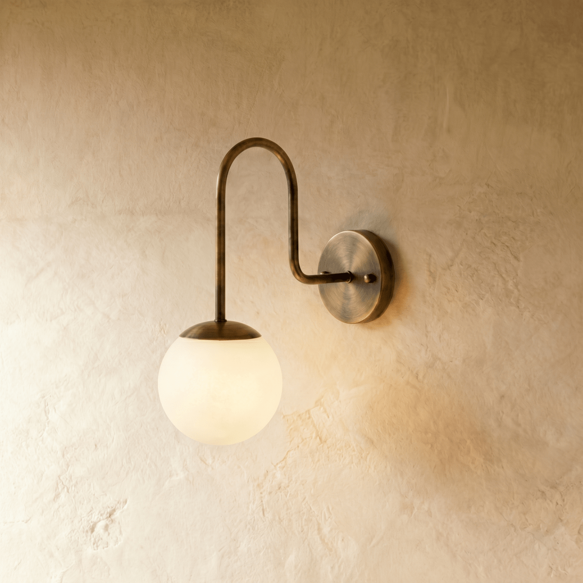 Clérachic wall lamp in vintage brass, a frosted glass globe glowing beneath a curved gooseneck arm.