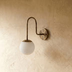 Clérachic wall lamp in vintage brass shown from another angle, the globe shade softly lit against plaster.