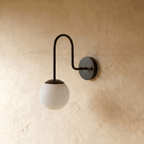 Clérachic wall lamp in matte black shown from another angle, the globe shade softly lit against plaster.