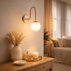 Clérachic wall lamp in brushed brass above a side table set with a candle and perfume bottles.