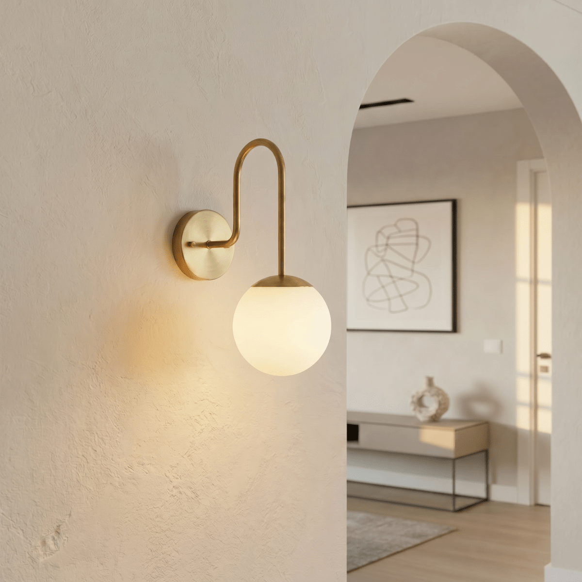 Clérachic wall lamp in brushed brass mounted by an archway leading into a bright entry hall.