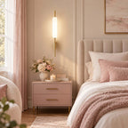Lit over a blush-pink bedside table with a vase of roses, this Clérachic brass wall sconce sits beside a ribbed pink headboard.