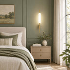 This Clérachic brass wall sconce glows against a sage-green panelled wall, above a light oak nightstand and a bed with olive bedding.