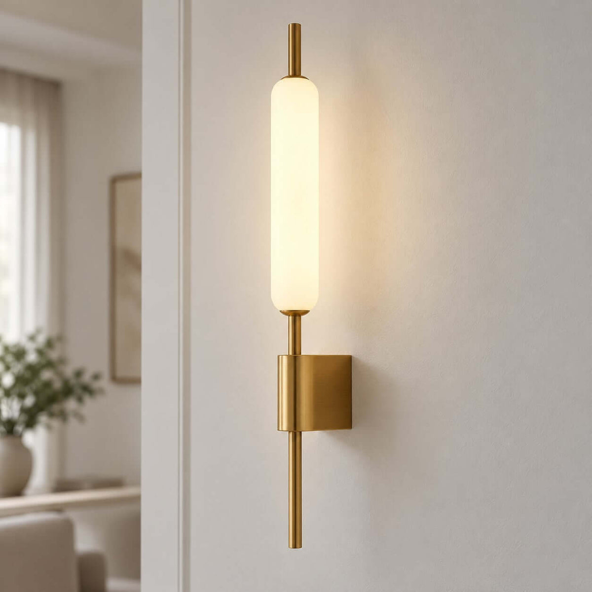 Close view of the lit frosted glass tube on this Clérachic brass wall sconce, mounted on a pale wall with a square back plate.