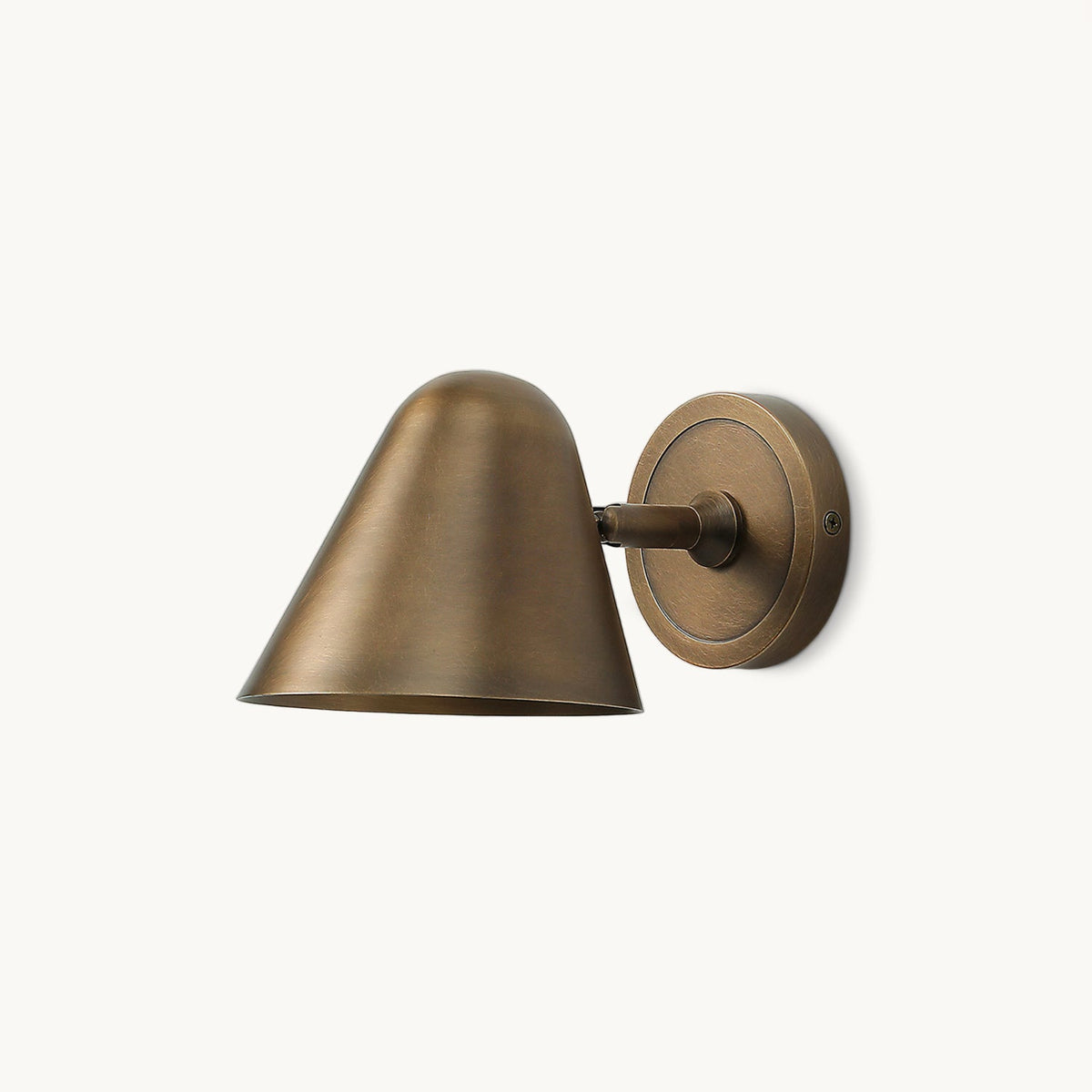 This Clérachic wall light on a plain white backdrop, with an antique brass cone shade on a short arm and a round brass backplate.