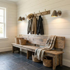 Three Clérachic antique brass wall lights along a white shiplap wall above a rustic bench, with a coat rack, baskets and a slate floor.
