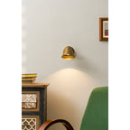 A Clérachic antique brass wall light on a pale wall above a painted cabinet, with a green chair and a small framed print nearby.