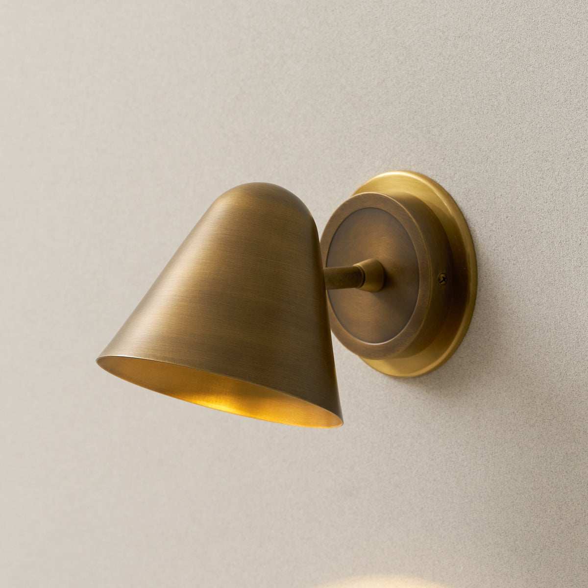 Three-quarter view of a Clérachic antique brass wall light, with the shade tilted down and its warm inner surface visible.