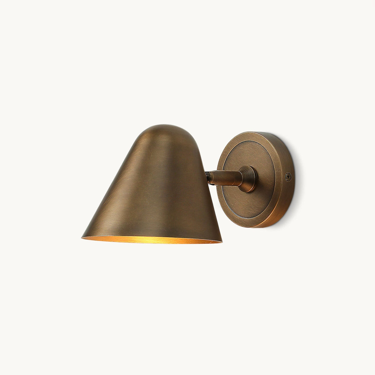 A Clérachic antique brass wall light with a round brass backplate on a plain white backdrop, seen from the side.