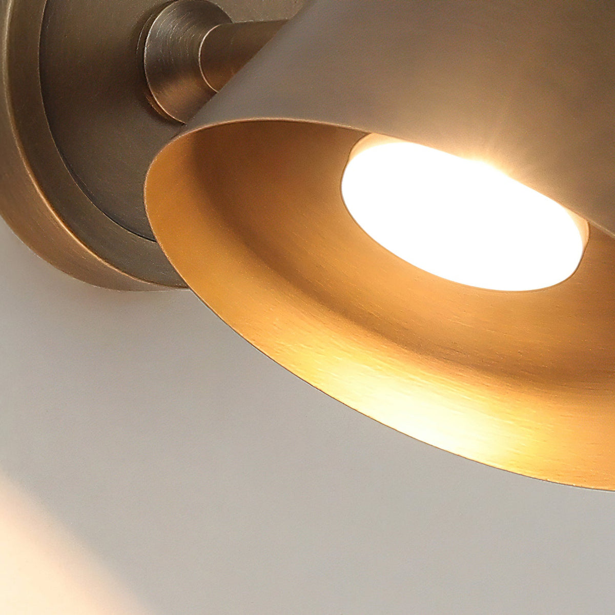 Close view from below of the glowing bulb and the warm brass inside of the cone shade on this Clérachic wall light.