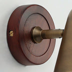 Close view of the round dark walnut-coloured backplate on this Clérachic wall light, with a brass screw and the brass arm base.