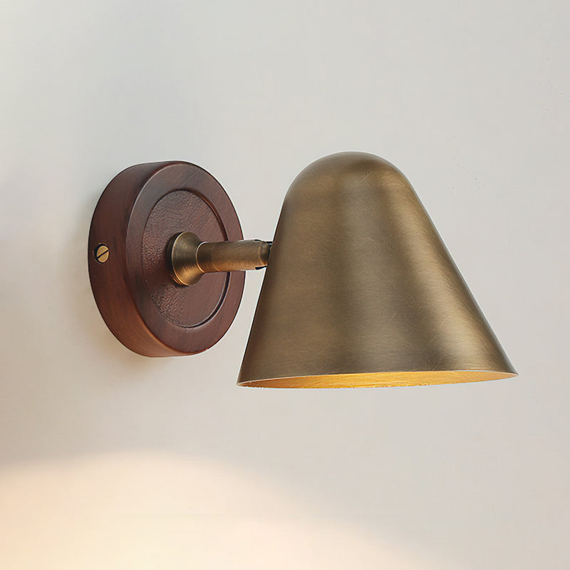 A Clérachic wall light with an antique brass cone shade on a round dark walnut-coloured backplate, lit on a pale wall.