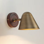 A Clérachic wall light with an antique brass cone shade on a round dark walnut-coloured backplate, lit on a pale wall.