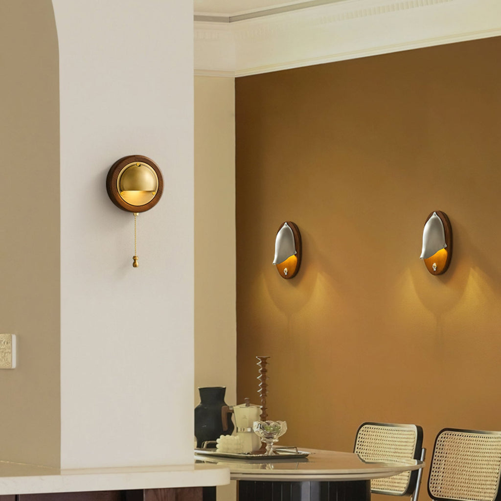 Wide view of a Clérachic round wall light on a cream pillar, with an amber dining area and two further lights in the background.