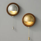 A round Walnut & Silver and a round Walnut & Brass Clérachic wall light side by side on a grey wall, each with its pull chain and knob.