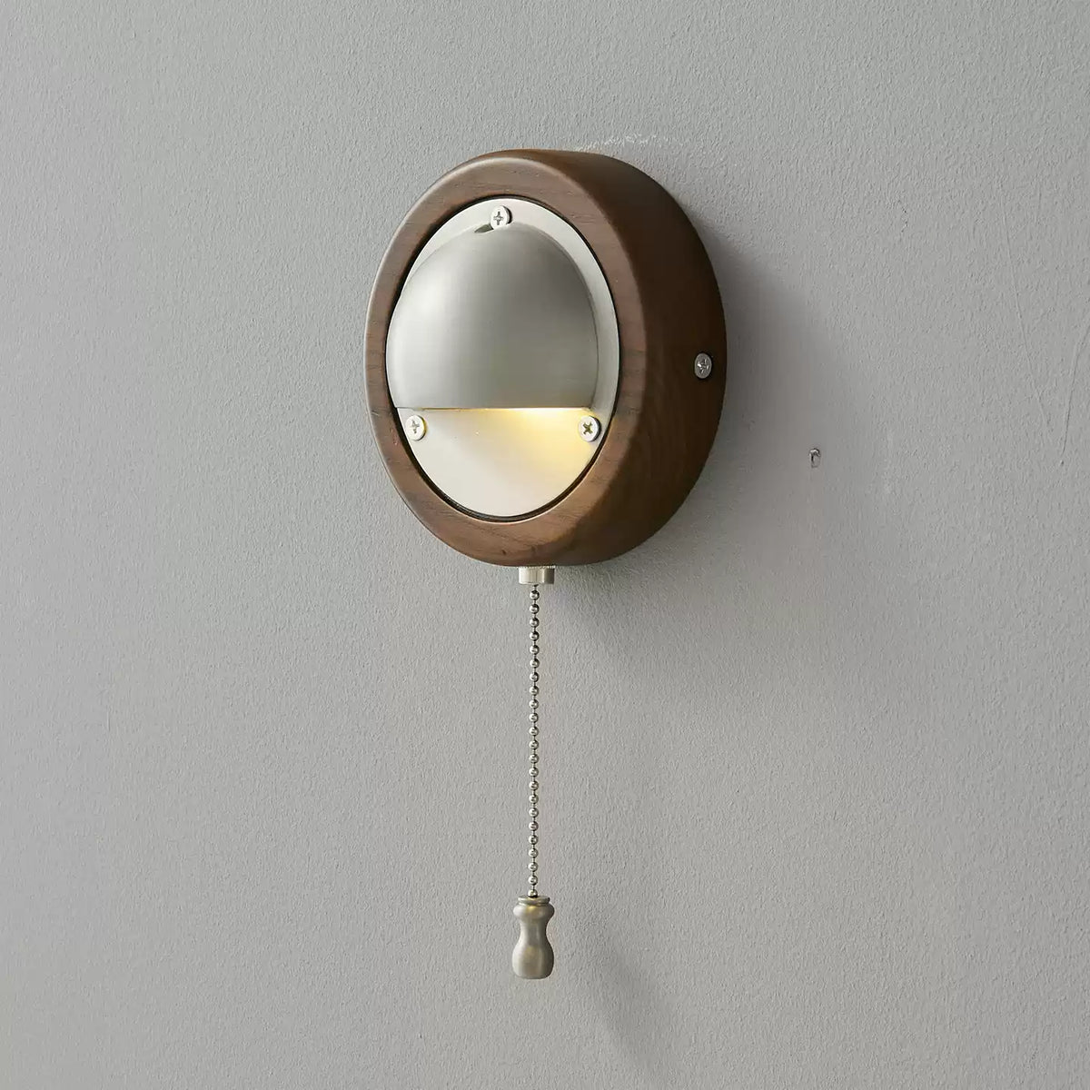 A round Walnut & Silver Clérachic wall light with a silver half-dome shade and a beaded pull chain, on a plain grey wall.