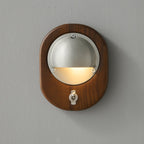 An oval Walnut & Silver Clérachic wall light on a grey wall, with warm light washing down from under the half-dome shade.