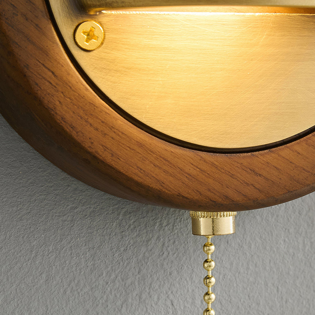 Close view of the brass half-dome glowing above a walnut frame, with the brass chain fitting below this Clérachic wall light.