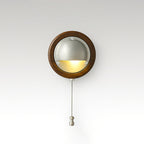 Round Walnut & Silver Clérachic wall light with a lit half-dome and a chain pull, on a soft grey studio backdrop.