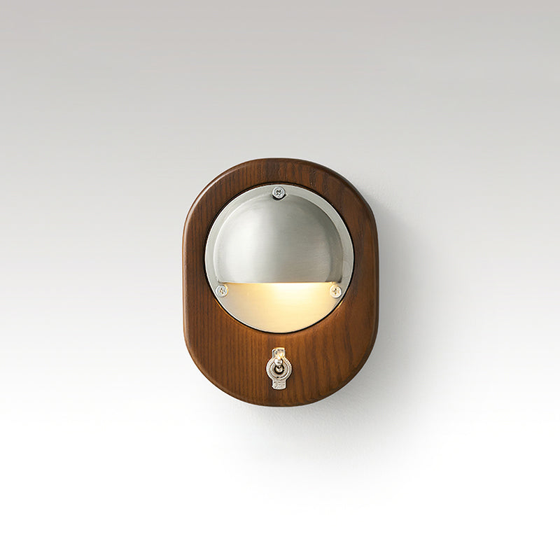 Oval Walnut & Silver Clérachic wall light with a toggle switch below the lit half-dome, on a soft grey studio backdrop.