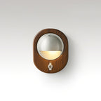 Oval Walnut & Silver Clérachic wall light with a toggle switch below the lit half-dome, on a soft grey studio backdrop.