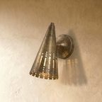 Clérachic wall lamp in vintage brass with a perforated cone shade casting warm striped light on the wall.