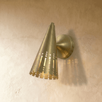Clérachic wall lamp in brushed brass, the perforated cone shade glowing with vertical light slats.