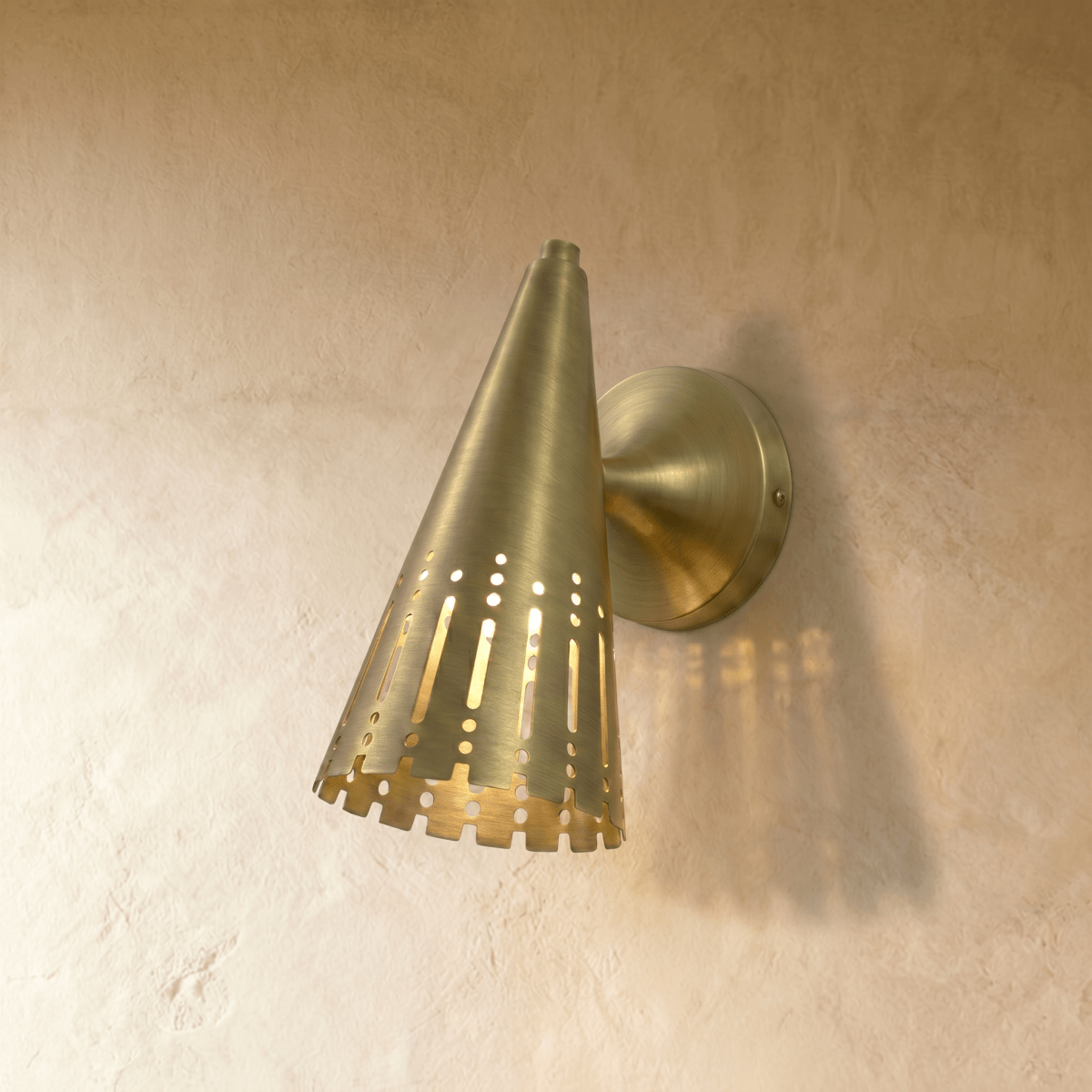 Clérachic wall lamp in brushed brass, the perforated cone shade glowing with vertical light slats.