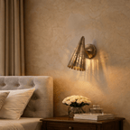 Clérachic wall lamp in vintage brass mounted above a bedside table with white roses and stacked books.