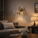 Clérachic wall lamp in vintage brass glowing above a sofa, paired with a table lamp and fresh flowers.