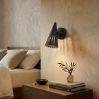 Clérachic wall lamp in matte black above a walnut nightstand with stacked design books and a small vase.